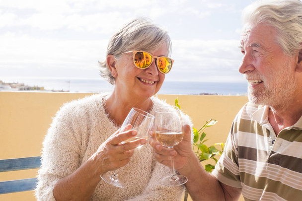 老夫婦が夏の海を見渡す屋外テラスでワインと乾杯 - 写真・画像