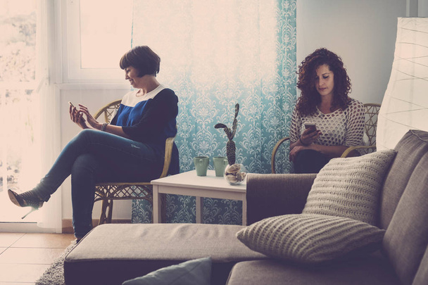 kaksi naista ystäviä kotona jokainen matkapuhelin chat ja katso tai tarkista sähköposti. Älkää puhuko toisillenne nykypäivänä. teknologia tuhota ystävyys käsite
 - Valokuva, kuva