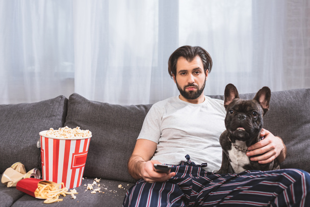 guapo solitario viendo tv con bulldog en sofá en sala de estar
  - Foto, Imagen