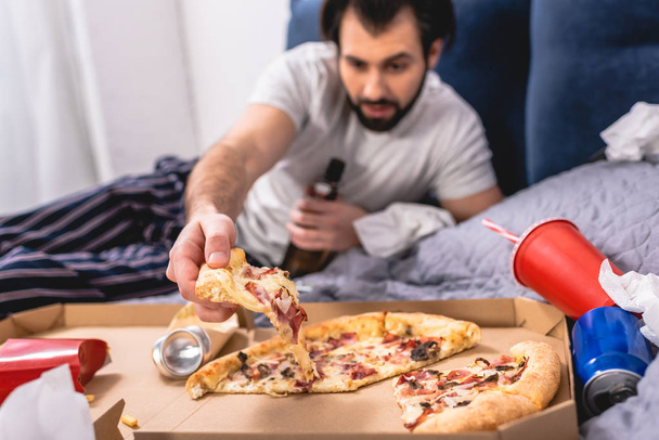 guapo solitario tomando pedazo de pizza en la cama en el dormitorio
 - Foto, imagen