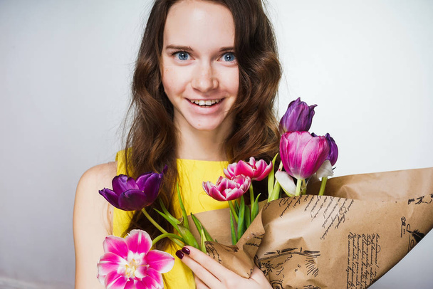 happy young blue-eyed girl in a yellow dress holding a bouquet of fragrant flowers - Foto, Imagem