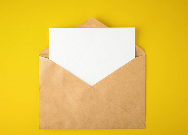 white paper card in an envelope on yellow background - Фото, изображение
