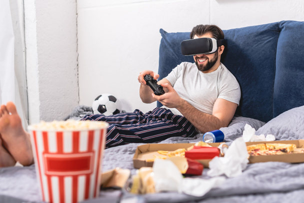 sonriente solitario usando auriculares de realidad virtual y jugando videojuego en el dormitorio
 - Foto, Imagen
