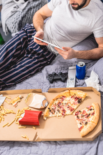 cropped image of loner using tablet with pizza on bed in bedroom - Fotografie, Obrázek