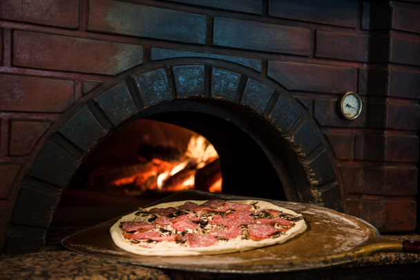 close up view of cooking process of raw pizza on wooden stove in brick oven - Foto, Bild
