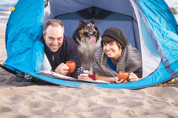 сімейний портрет для альтернативного відпочинку влітку на пляжі з наметом. приємно і посміхається чоловік і жінка з прикордонним собакою-колі посередині, як син. концепція щастя і свободи під сонячним світлом
 - Фото, зображення