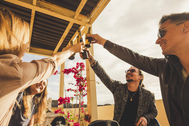 nuoret valkoihoiset miehet ja vaaleat naiset juhlivat menestystä ulkona terassilla juomalla olutta ja pitämällä hauskaa yhdessä
 - Valokuva, kuva