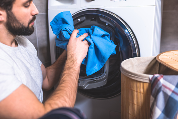 side view of loner putting laundry in washing machine in bathroom - Photo, Image