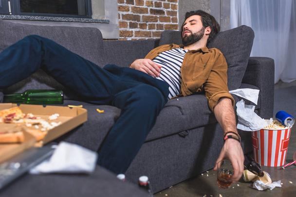  loner sleeping on sofa with glass of whiskey in dirty living room - Photo, Image
