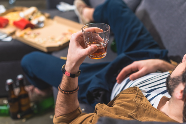 cropped image loner lying on sofa with glass of whiskey at living room - Foto, Bild