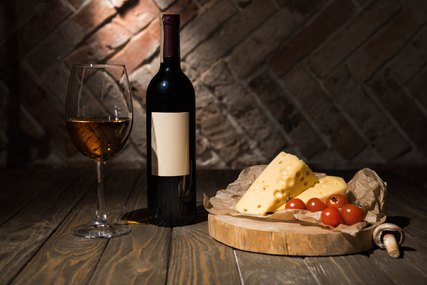 zblízka pohled láhve a sklenky vína se sýrem a veselé rajčata na pečící papír na dřevěné dekorativní pařez - Fotografie, Obrázek