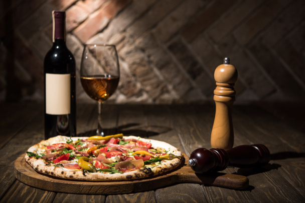 selective focus of italian pizza, spices in grinders, bottle and glass of wine on wooden tabletop - Photo, Image