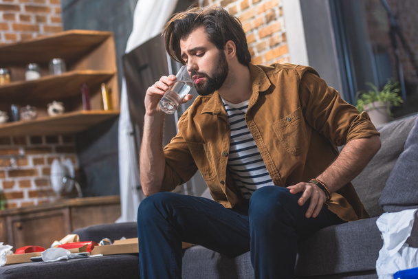 handsome loner drinking water while having hangover in morning at living room - Photo, Image