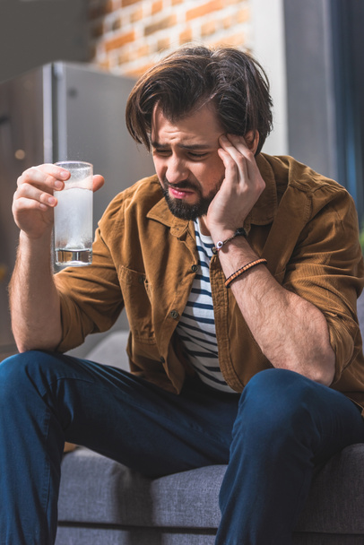 handsome loner holding glass of water with pill and having headache at living room - Foto, immagini