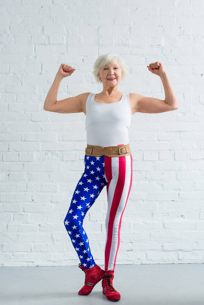 happy senior woman in sportswear showing muscles and smiling at camera - 写真・画像