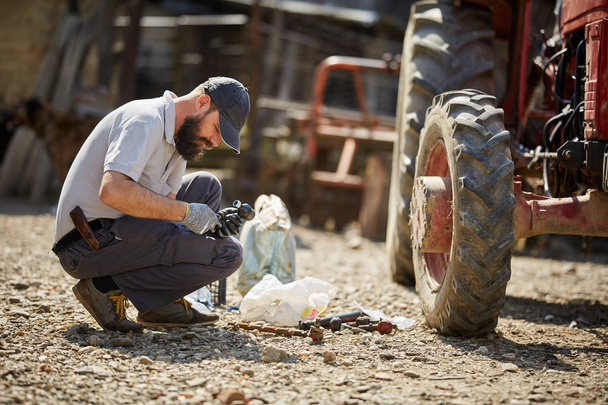 Young farmer repairing his tractor in sunny day - Foto, imagen