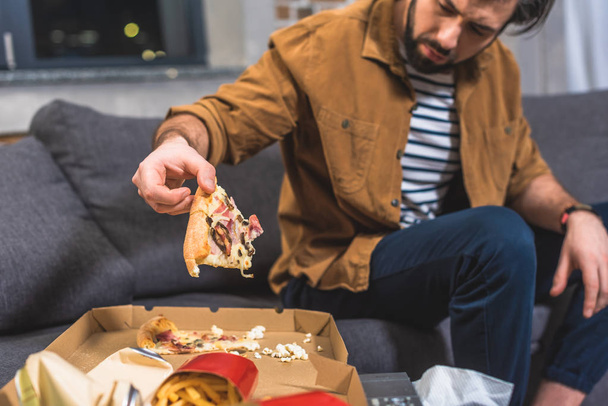 cropped image of angry loner taking piece of pizza at living room - Foto, Bild