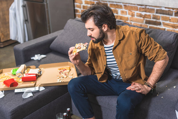 handsome loner eating pizza at living room - Foto, afbeelding
