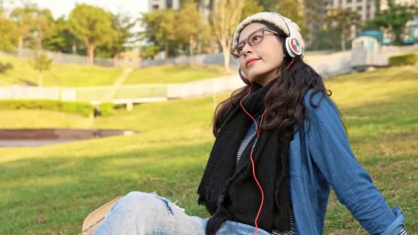 bela jovem mulher da Ásia usando o smartphone com fone de ouvido ouvir música no parque da cidade
. - Filmagem, Vídeo