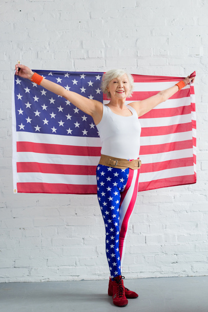 Gelukkig senior Sportvrouw houden van de Amerikaanse vlag en lachend op camera  - Foto, afbeelding