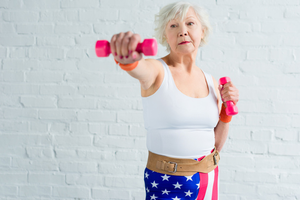 активная старшая женщина упражняется с гантелями и смотрит в сторону
 - Фото, изображение