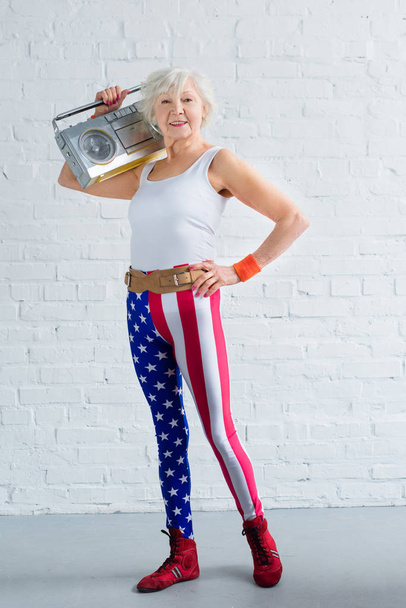 happy senior woman in sportswear holding tape recorder and smiling at camera - Foto, imagen