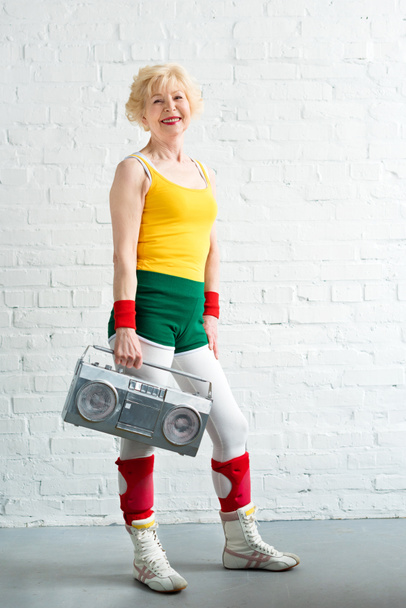 beautiful sportive senior woman holding tape recorder and smiling at camera  - Fotoğraf, Görsel