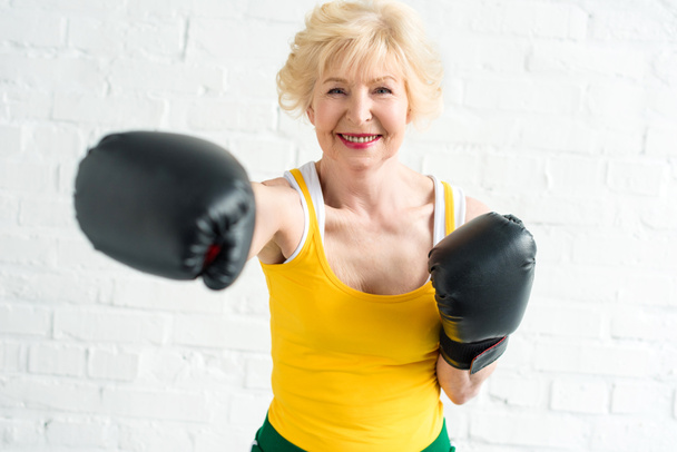 heureuse femme âgée dans la formation de gants de boxe et souriant à la caméra
 - Photo, image