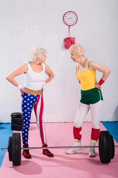 Seniorinnen stehen mit Händen in der Taille und lächeln sich im Fitnessstudio an - Foto, Bild