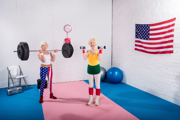 üst düzey sportswomen dumbell ve halter salonunda egzersiz gülümseyen, yüksek açılı görünüş - Fotoğraf, Görsel