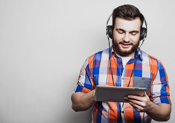 Studio portrait of a handsome bearded man using a tablet with headphones over a light grey  background. - Photo, Image