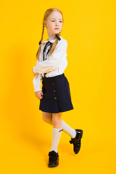 Κορίτσι με κόκκινο κοτσίδες σε κίτρινο φόντο. όμορφο κορίτσι στέκεται με το πόδι της. - Φωτογραφία, εικόνα