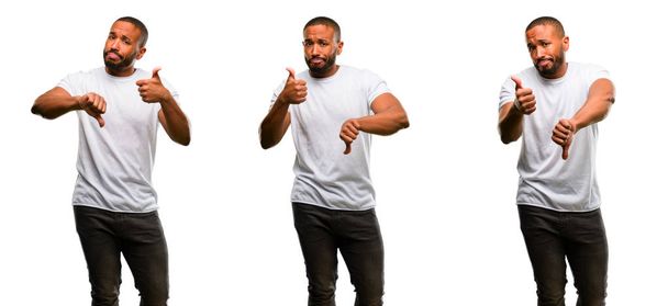 Αφρικανική αμερικανική άνδρα με μούσι συγχέεται με τους αντίχειρες επάνω και κάτω, προσπαθώντας να λάβει μια απόφαση που εκφράζουν την αμφιβολία και την απογοήτευση - Φωτογραφία, εικόνα