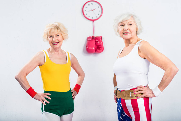 happy senior sportswomen standing with hands on waist and smiling at camera - 写真・画像