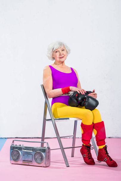 beautiful sportive senior woman with boxing gloves sitting and smiling at camera  - Photo, Image
