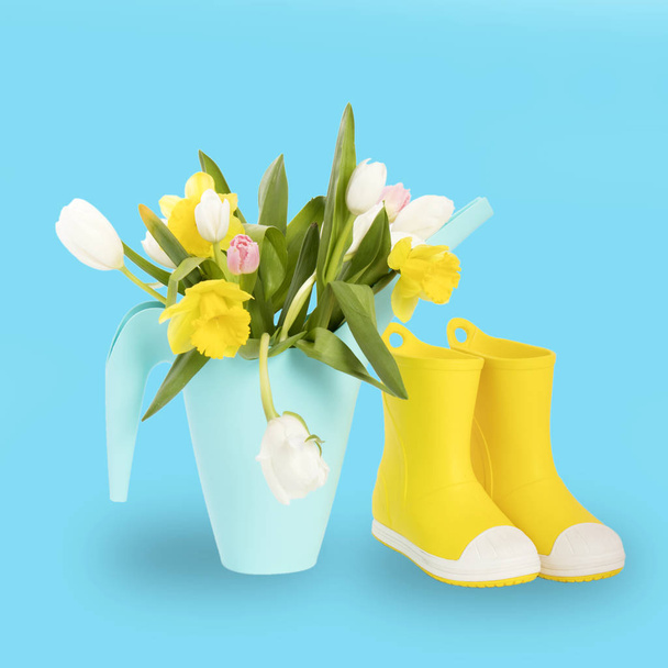 the Yellow rubber boots with a bouquet of flowers of yellow daffodils and white and pink tulips on white wooden table on the violet background. Garden accessories. - Φωτογραφία, εικόνα