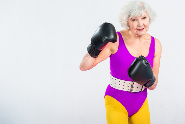sportive senior lady boxing and smiling at camera isolated on grey - Foto, imagen