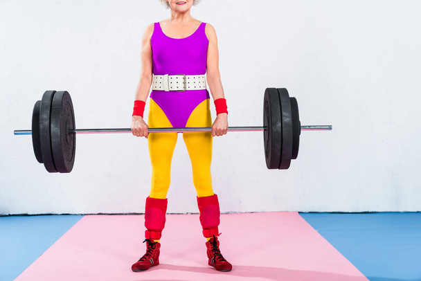 cropped shot of smiling senior woman in sportswear lifting barbell - Photo, Image