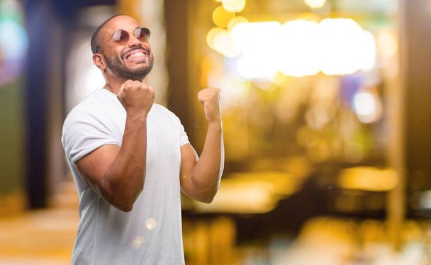 African american man with beard happy and excited celebrating victory expressing big success, power, energy and positive emotions. Celebrates new job joyful at night - Photo, Image