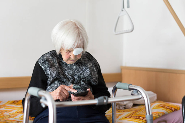 Lonley пожилая 95-летняя женщина сидит в плохом состоянии с помощью современного мобильного телефона
. - Фото, изображение