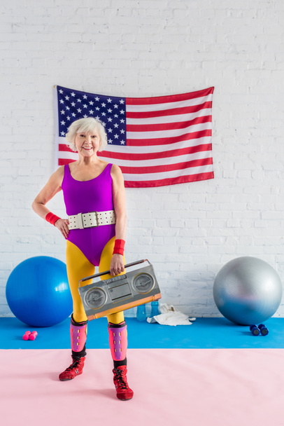 happy sporty senior woman holding tape recorder and smiling at camera - Photo, Image
