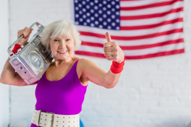 happy senior woman in sportswear holding tape recorder and showing thumb up - Foto, immagini