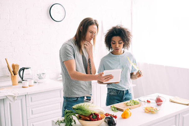 multikulturális fiatal pár látszó-nél recept digitális tabletta, és főzés a konyhában  - Fotó, kép