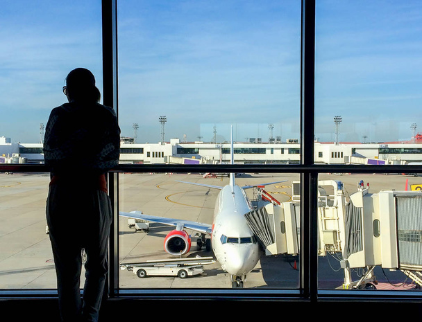 Silhouette eines Passagiers, der im Terminal vor dem Hintergrund des Flugzeugs auf eine Reise wartet - Foto, Bild