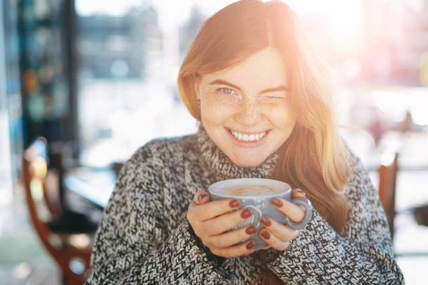 Bir fincan kahve tutan bir kapalı göz ile neşeli genç kadın - Fotoğraf, Görsel