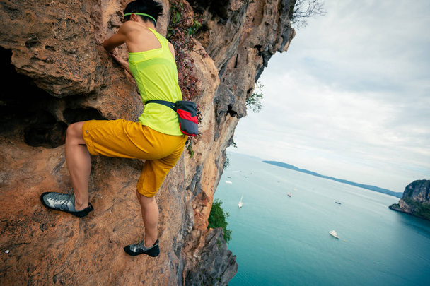 female rock climber climbing on seaside cliff - Photo, Image