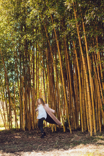 stylish young woman in a pink coat walking in a park next to bamboo trees, happy spring - Foto, immagini