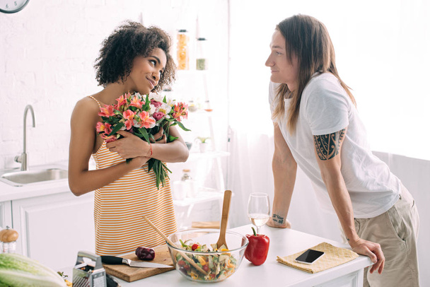 happy young african american woman holding bouquet of flowers and looking at boyfriend  - Photo, Image
