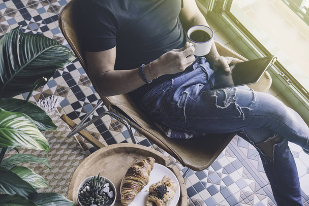 Handsome stylish man in headphones listening to music on electronic tablet and drinking cup of coffee at home. Casual relaxing and rest time concept. Blurred background.Visual effects. - Valokuva, kuva