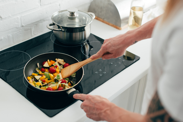 tiro recortado de hombre cocinar verduras en sartén en la estufa eléctrica
 - Foto, Imagen